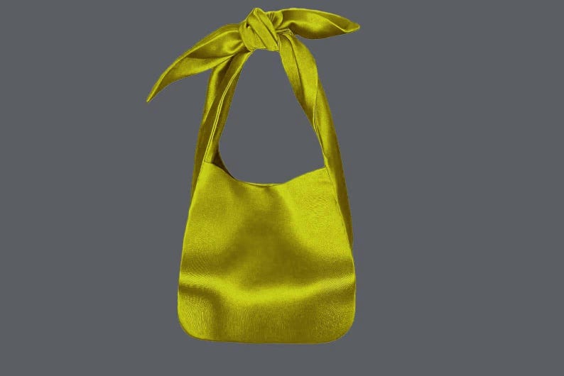 May include: A chartreuse-colored shoulder bag with a knotted handle. The bag has a soft, textured appearance and a rounded bottom. The background is a solid gray.