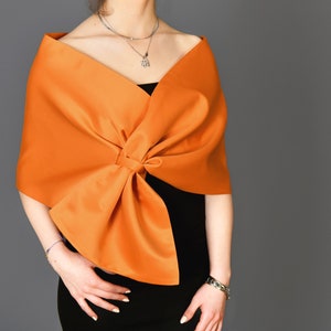 May include: A bright orange shawl with a large bow at the front. The shawl is made of a soft, silky fabric.