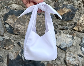 May include: A white fabric tote bag with a knotted handle. The bag is made of a smooth, silky material.