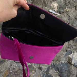 Op de afbeelding: Een magenta velvet clutch met een zwart interieur en een magnetische sluiting. De clutch heeft een afneembare polsband.