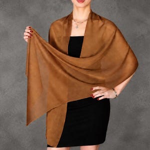 May include: A solid brown rectangular shawl made of a lightweight, semi-sheer fabric. The shawl is draped over the shoulders and across the front of the torso, showcasing its smooth texture and consistent earthy brown color throughout the material.