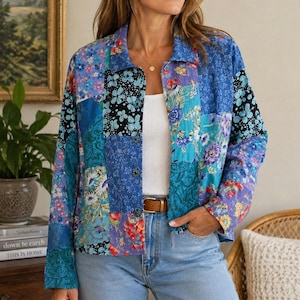 May include: A long-sleeved button-down jacket featuring a patchwork design with various blue, purple, and white floral and geometric patterns. The jacket has a collar, a front button closure, and is worn over a plain white top and light blue jeans.