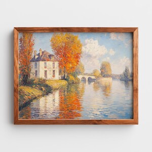 Könnte beinhalten: Gerahmtes Landschaftsgemälde, das eine ruhige Flussszene mit einem weißen Haus, einer Brücke und Bäumen in Herbstfarben zeigt. Das Kunstwerk ist in einem Holzrahmen gefasst und zeigt einen klassischen, impressionistischen Stil mit Reflexionen im Wasser.