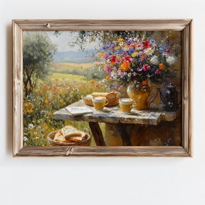 May include: A framed painting depicts a serene outdoor scene. A table is set with coffee cups, bread, and a vase of colorful flowers. The background shows a field and trees, with a soft, natural light.