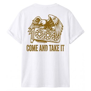 May include: A white short-sleeved t-shirt featuring a gold-colored graphic on the back. The design depicts a bald eagle perched atop a triple-fan graphics card, with the text "COME AND TAKE IT" printed in a distressed font underneath the image.