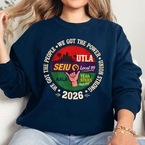 May include: Navy blue sweatshirt with a circular graphic. The graphic includes text that reads "WE GOT THE POWER" and "UNION STRONG". The graphic also features the text "UTLA", "SEIU Local 99", "TEAMSTERS Local 2010", and "2026".