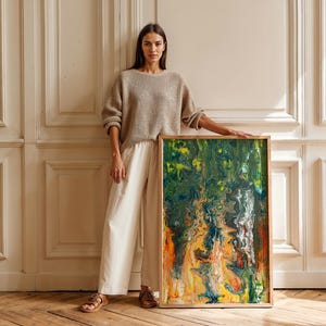 May include: An abstract painting with a wooden frame. The artwork features a vibrant mix of colors, including green, yellow, orange, and blue, creating a dynamic and textured composition. The painting is displayed against a white wall and wooden floor.