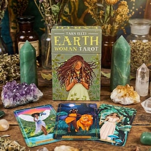 May include: A tarot card deck titled "Earth Woman Tarot" with illustrations of women and nature. The box features a woman holding a plant. Three tarot cards are displayed, along with crystals and other decorative items.