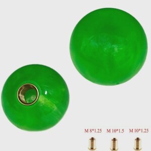 Peut inclure: Deux boutons sphériques verts avec une finition brillante. L'un des boutons a un insert fileté en laiton. Trois inserts filetés en laiton sont affichés en dessous des boutons, avec le texte "M 8*1.25 M 10*1.5 M 10*1.25".