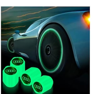 May include: A sleek silver car with illuminated green wheel rims and four glowing green valve caps. The caps display the Audi logo. The image conveys a sense of speed and modern automotive design, with the green lights.