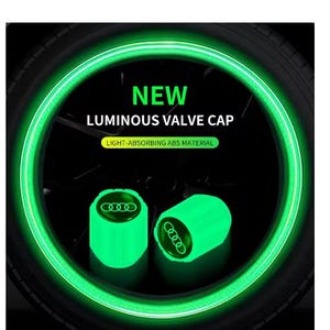 May include: Two luminous green valve caps with the Audi logo are displayed, emitting a bright glow. The caps are set against a dark background, with a glowing green tire rim in the background. Text reads "NEW LUMINOUS VALVE CAP".