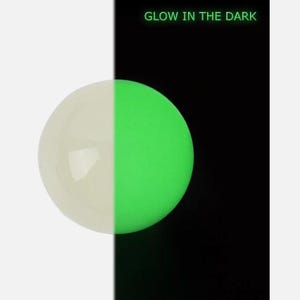 Op de afbeelding: Een bol, half wit en half groen oplichtend, tegen een zwart-witte achtergrond. De tekst "GLOW IN THE DARK" is weergegeven. De groene kant van de bol is verlicht.