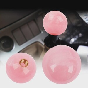Pode incluir: Três manípulos de câmbio de carro rosa e esféricos. Dois manípulos são sólidos, enquanto um tem uma inserção rosqueada de latão. Os manípulos têm uma aparência marmorizada. Fundo desfocado.
