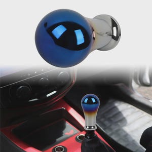 Op de afbeelding: Een blauw en chroom schakelpookknop met een bolvormige bovenkant. De knop heeft een kleureffect, dat overloopt van blauw naar geel. De basis is chroom en de knop is ontworpen voor de versnellingspook van een auto.