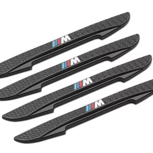 May include: Four black car door sill protectors with a textured surface. Each has the "M" logo with blue, red, and white stripes. These protectors are designed to shield door sills from scratches and damage. Each measures approximately 40 cm in length.