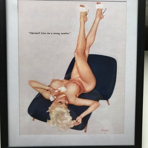 May include: A framed vintage-style pin-up illustration featuring a blonde figure reclining on a dark blue chair while holding a white telephone receiver. The text reads, "Operator? Give me a wrong number." The figure wears white high-heeled shoes.