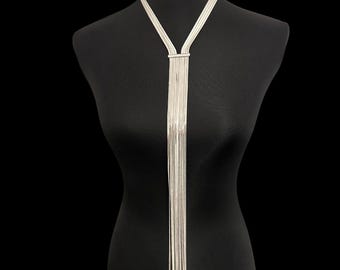 以下が含まれることがあります： Y字型のデザインのシルバーカラーのネックレス。ネックレスは、長方形の留め金から連なる繊細なチェーンの複数のストランドが特徴です。ジュエリーは、黒い背景に対して黒いマネキンに表示されています。