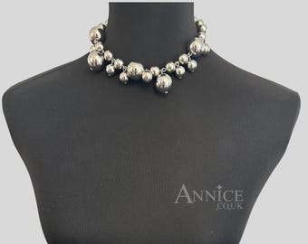May include: A silver-toned choker necklace featuring a cluster of polished spherical beads of varying sizes suspended from a central chain. The necklace is displayed on a black mannequin bust with the text Annice.co.uk visible in the bottom right corner.