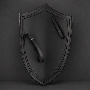 May include: A black shield with a pointed bottom and rounded top. The shield has a dark, matte finish and is edged with a raised border. Two black leather straps are attached to the back for holding. Rivets secure the border and straps.