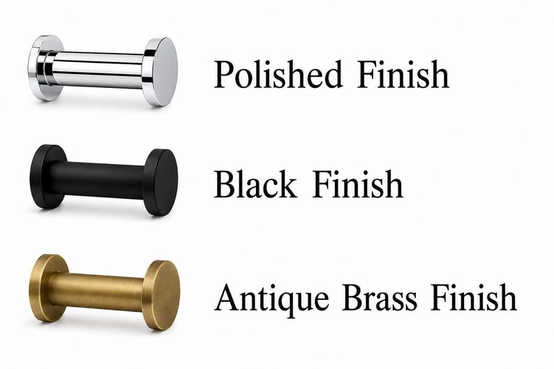 K&ouml;nnte beinhalten: Drei zylindrische Wandhaken mit flachen, runden Enden, die in einer vertikalen Reihe angeordnet sind. Der obere Haken hat ein gl&auml;nzendes, silbernes Polished Finish, der mittlere ein mattes Black Finish und der untere ein metallisches Antique Brass Finish.