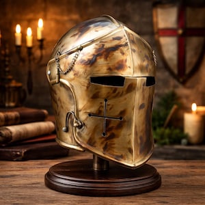 Può includere: Un elmo da cavaliere medievale color ottone con un disegno a croce, esposto su un supporto di legno. L'elmo presenta una visiera con fessure per gli occhi e un dettaglio a catena. Lo sfondo include candele e uno scudo.