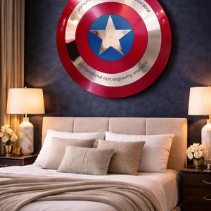 Puede incluir: Un escudo grande y redondo con un dise&ntilde;o rojo y plateado, con una estrella azul en el centro. El escudo tiene el texto "personalized text engraving available" alrededor del borde. Est&aacute; montado en una pared azul oscuro sobre una cama.