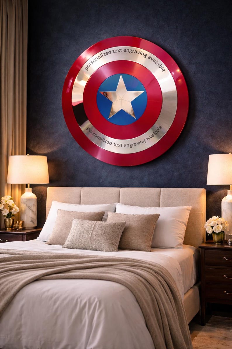 Puede incluir: Un escudo grande y redondo con un dise&ntilde;o rojo y plateado, con una estrella azul en el centro. El escudo tiene el texto "personalized text engraving available" alrededor del borde. Est&aacute; montado en una pared azul oscuro sobre una cama.