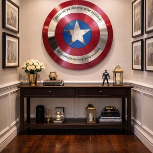Puede incluir: Una exhibici&oacute;n decorativa de pared con un gran escudo con un anillo exterior rojo y plateado, un centro azul y una estrella plateada. El texto "personalized text engraving avalable" est&aacute; impreso en el escudo. Una consola de madera oscura debajo.