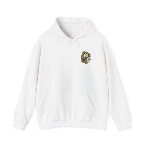 Könnte beinhalten: Ein weißer Kapuzenpullover mit einer kleinen Grafik auf der linken Brust. Die Grafik zeigt ein Cartoon-Opossum, das an einem grünen Ast hängt, mit dem Text "STAY WEIRD" in schwarzen Buchstaben daneben, ergänzt durch ein kleines schwarzes Herz.
