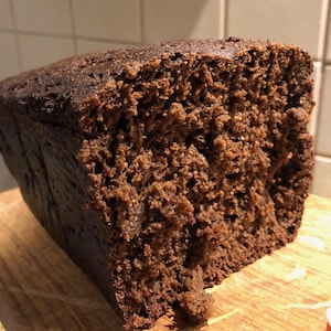 May include: A dark brown loaf of bread, freshly baked with a textured, porous interior. The bread has a slightly rough crust and a dense, moist crumb. The cut reveals the soft, airy inside, suggesting a rustic style.