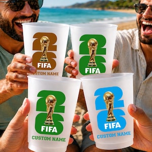May include: Four clear plastic cups with a FIFA World Cup design. Each cup features the number 26, a gold trophy, the word FIFA, and the text "CUSTOM NAME" in a different colour: brown, green, green, and blue.