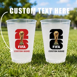 May include: Two clear plastic cups with a FIFA logo and the text "CUSTOM TEXT HERE". One cup has a red background, the other black. Both feature a gold trophy and space for a custom name.