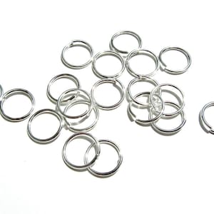 May include: A group of silver jump rings, a type of jewellery finding, scattered on a white surface.