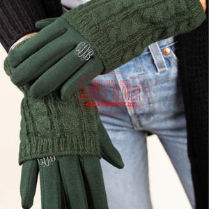 May include: Dark green gloves with a cable knit cuff and a smooth palm. Each glove features a silver-colored monogram ring. The gloves are designed for warmth and style.