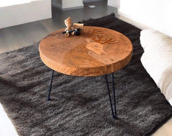 Könnte beinhalten: Ein runder Couchtisch aus Holz mit einem Hirsch-Schnitzmuster. Er hat schwarze Metall-Haarnadelbeine und steht auf einem dunkelgrauen Shaggy-Teppich. Dekorative Gegenstände sind auf dem Tisch platziert.