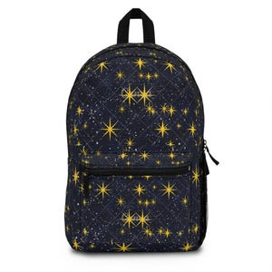 Peut inclure: Un sac à dos bleu marine foncé avec un motif matelassé en losanges et un imprimé d'étoiles jaunes à quatre branches et de petits points blancs. Le sac comprend une poignée supérieure, une poche frontale zippée et une poche latérale en filet noir.