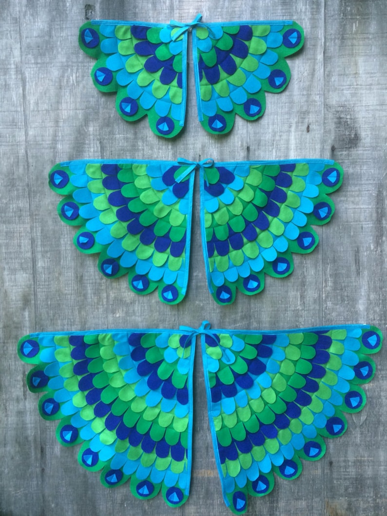 May include: Three pairs of peacock wings made of felt. The wings are in different sizes and are layered on top of each other. The wings are blue, green, and teal.
