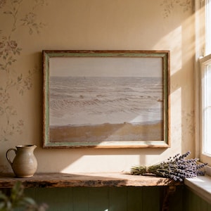Może przedstawiać: Oprawiony wydruk przedstawiający krajobraz morski z postarzaną zielono-brązową drewnianą ramą. Grafika przedstawia stonowaną, monochromatyczną scenę oceanu. Rustykalna drewniana półka mieści ceramiczny dzbanek, pęczek lawendy i bukiet suszonej trawy.