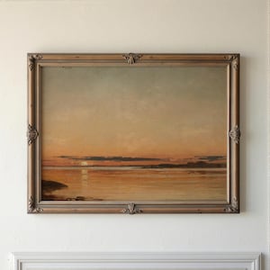 May include: An antique landscape painting depicting a sunset over water, framed in a decorative wooden frame. The artwork features warm tones of orange, gold, and brown, with a soft, diffused light reflecting on the water's surface. The frame has ornate corner details.