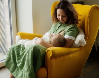 May include: A woman in a green dress sits in a yellow armchair and breastfeeds a baby.