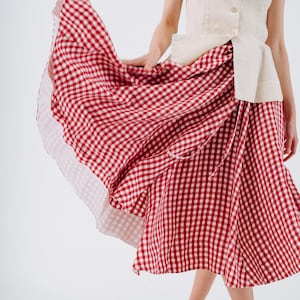 May include: A sleeveless, cream-colored top with a high collar and button closure paired with a red and white checkered skirt. The skirt is flowing, and the hem is visible. Tan shoes complete the outfit.