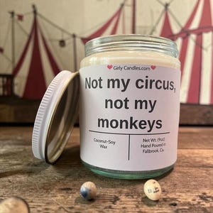 May include: A glass jar candle with a white label that reads "Not my circus, not my monkeys." The candle is open, revealing the wax inside. The background features a circus tent design. The candle is 9oz.