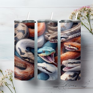 Peut inclure: Trois gobelets cylindriques présentant une impression continue de divers serpents dans des tons orange, bleu, blanc et marron. Chaque gobelet comprend un couvercle transparent et une paille blanche, mettant en valeur des écailles détaillées.
