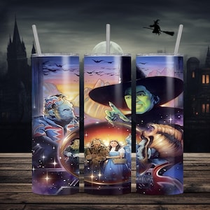 Puede incluir: Tres vasos de acero inoxidable con el tema de El Mago de Oz. Cada vaso presenta un personaje o escena diferente de la película, incluyendo el Hombre de Hojalata, la Bruja Malvada y Dorothy. El fondo incluye un castillo, una luna y murciélagos.