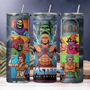 Könnte beinhalten: Ein Edelstahlbecher mit einem Comic-Design mit Charakteren aus Masters of the Universe. Das Design umfasst He-Man, Skeletor und andere Charaktere mit den Worten "Masters of the Universe". Der Becher hat einen silbernen Strohhalm.