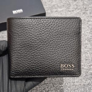 May include: A black bi-fold wallet with a textured, pebbled leather surface. The bottom right corner features a metallic silver-toned BOSS logo plate. The wallet is presented alongside a matching black box with the BOSS logo printed in white.