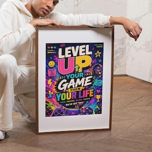 May include: A framed poster with the text "LEVEL UP YOUR GAME THEN YOUR LIFE" in bright colours. The poster features gaming graphics, including controllers and headphones. The frame is a dark brown colour.