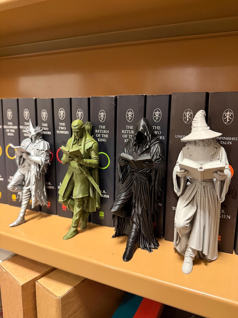 May include: Four figurines of characters from a fantasy novel, each holding a book. The figures are in silver, olive green, black, and gray. The figurines are displayed in front of a row of books with the title "The Lord of the Rings".