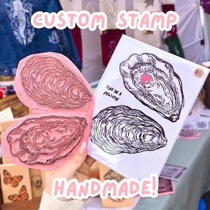 May include: A handmade custom stamp featuring a pink oyster design. Beside it is a print with two oyster illustrations and the text "ONE IN A MILLION". The words "CUSTOM STAMP" and "HANDMADE!" are also visible.