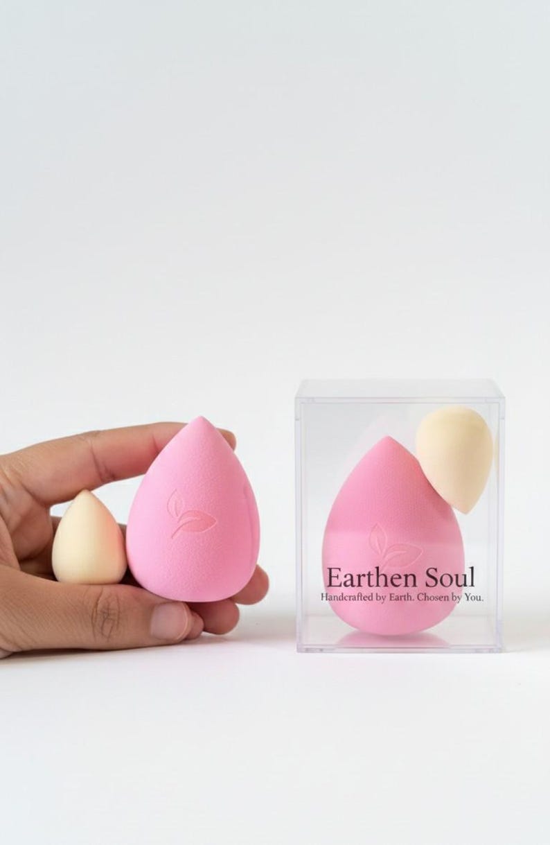 May include: Pink and beige teardrop-shaped makeup sponges. One large pink sponge has a leaf design. The text "Earthen Soul" is on the clear box containing a pink sponge and a beige sponge. The sponges are for applying makeup.